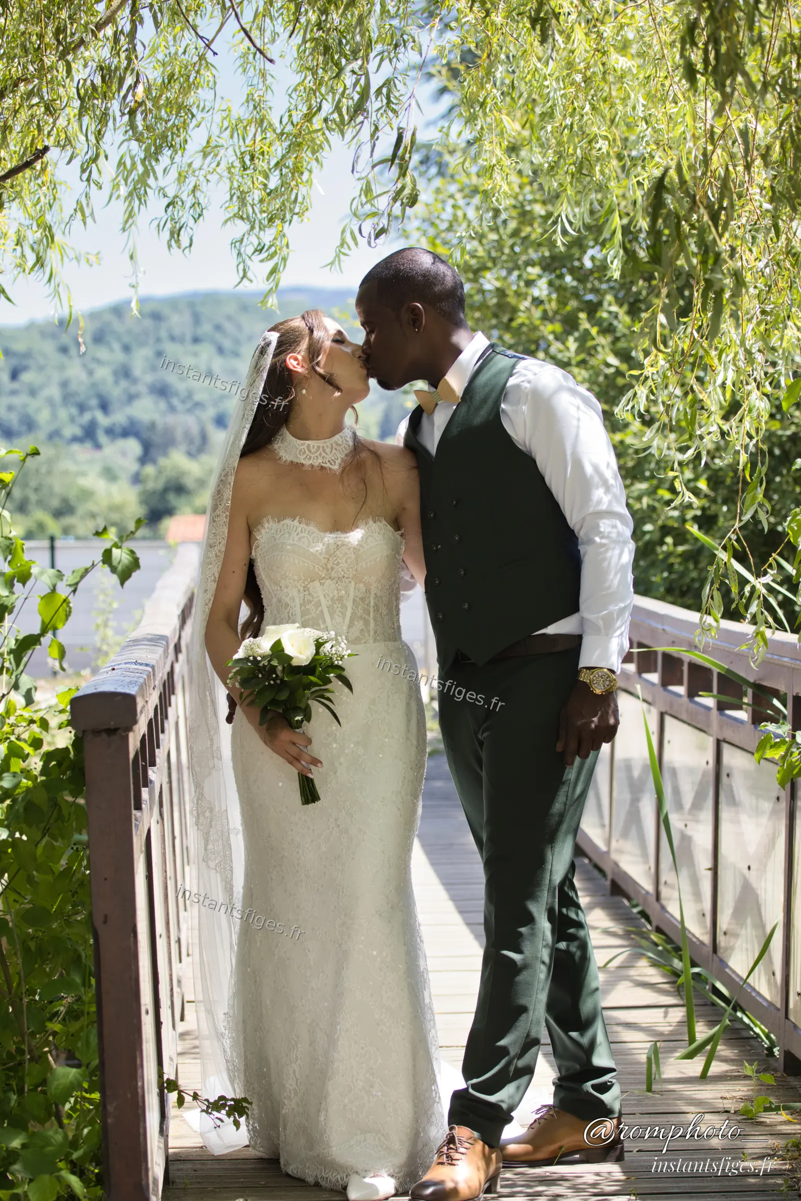 Baiser des mariés sur un pont en bois entouré de verdure, au-dessus d'une rivière, Mariage Seine-et-Marne